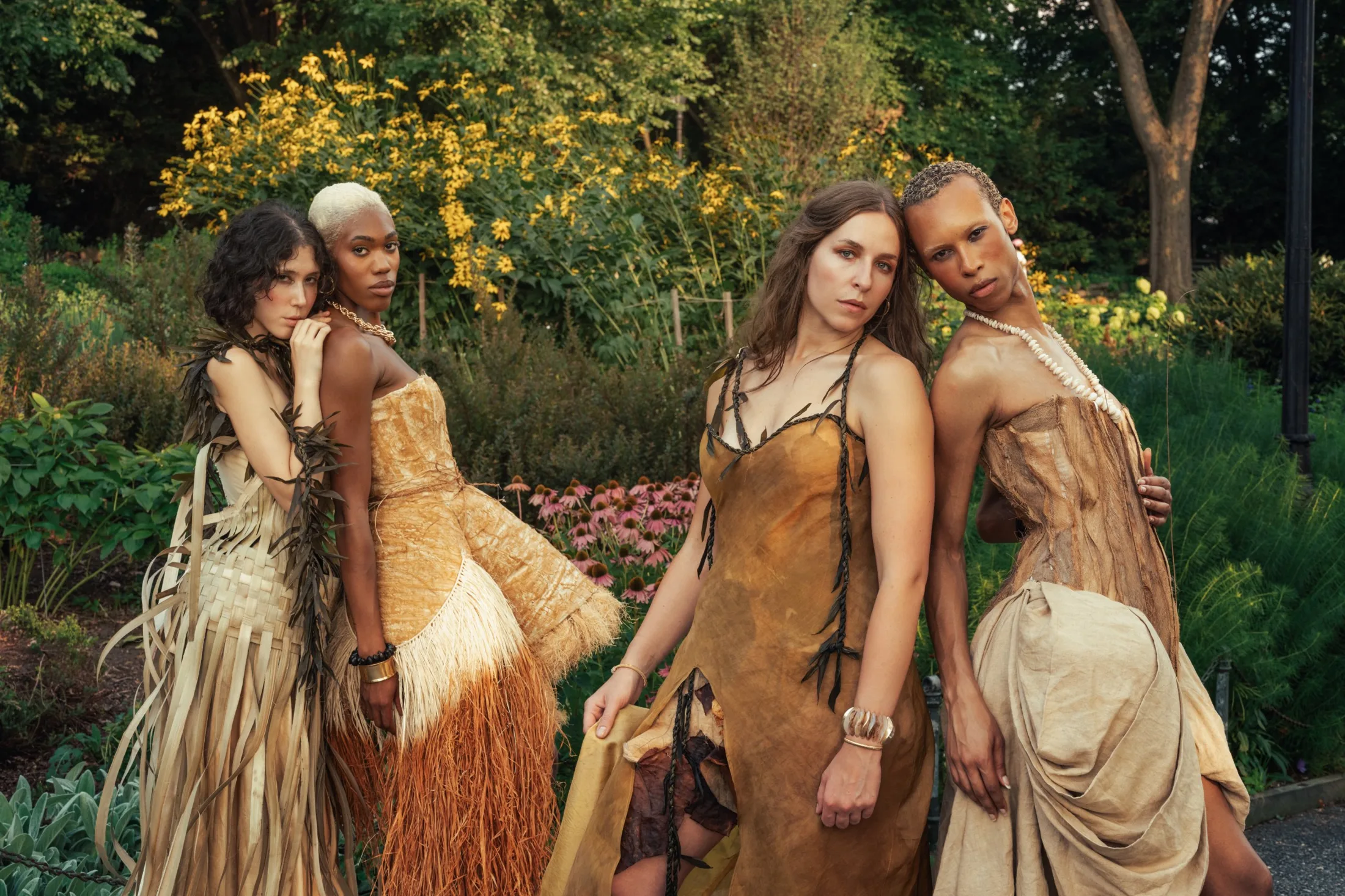 Four models in natural-fiber gowns in a summer garden