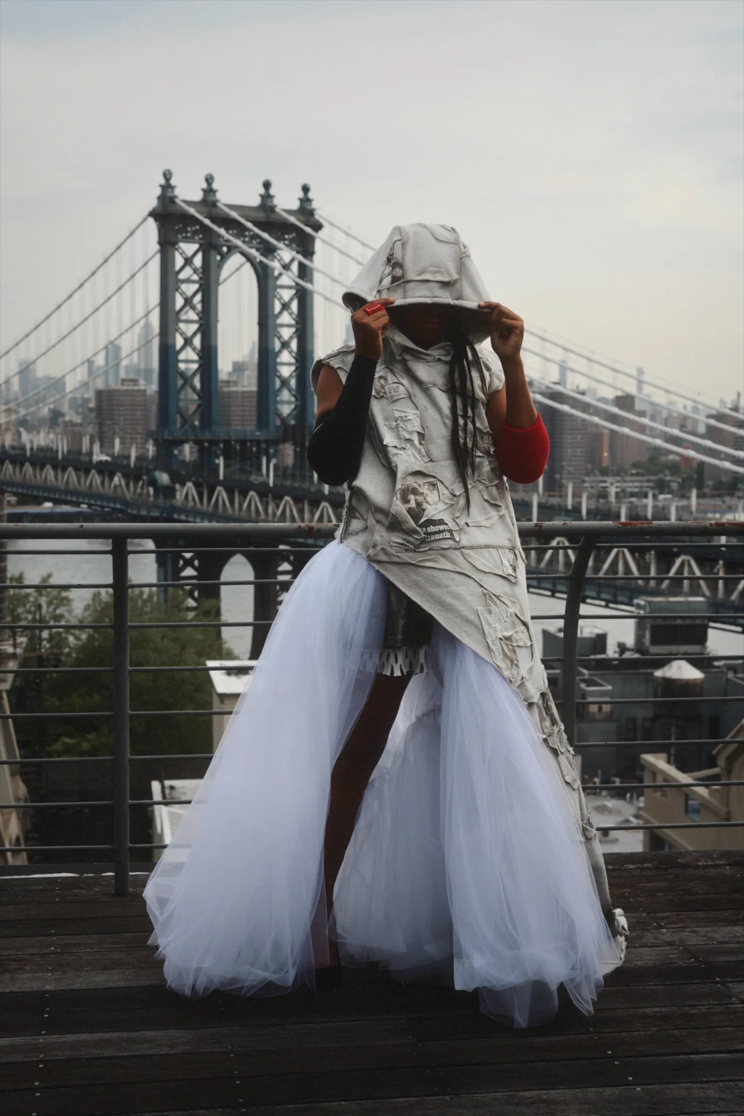 Naomi Osaka in a hooded collaged jersey top over white tulle with the Manhattan Bridge behind