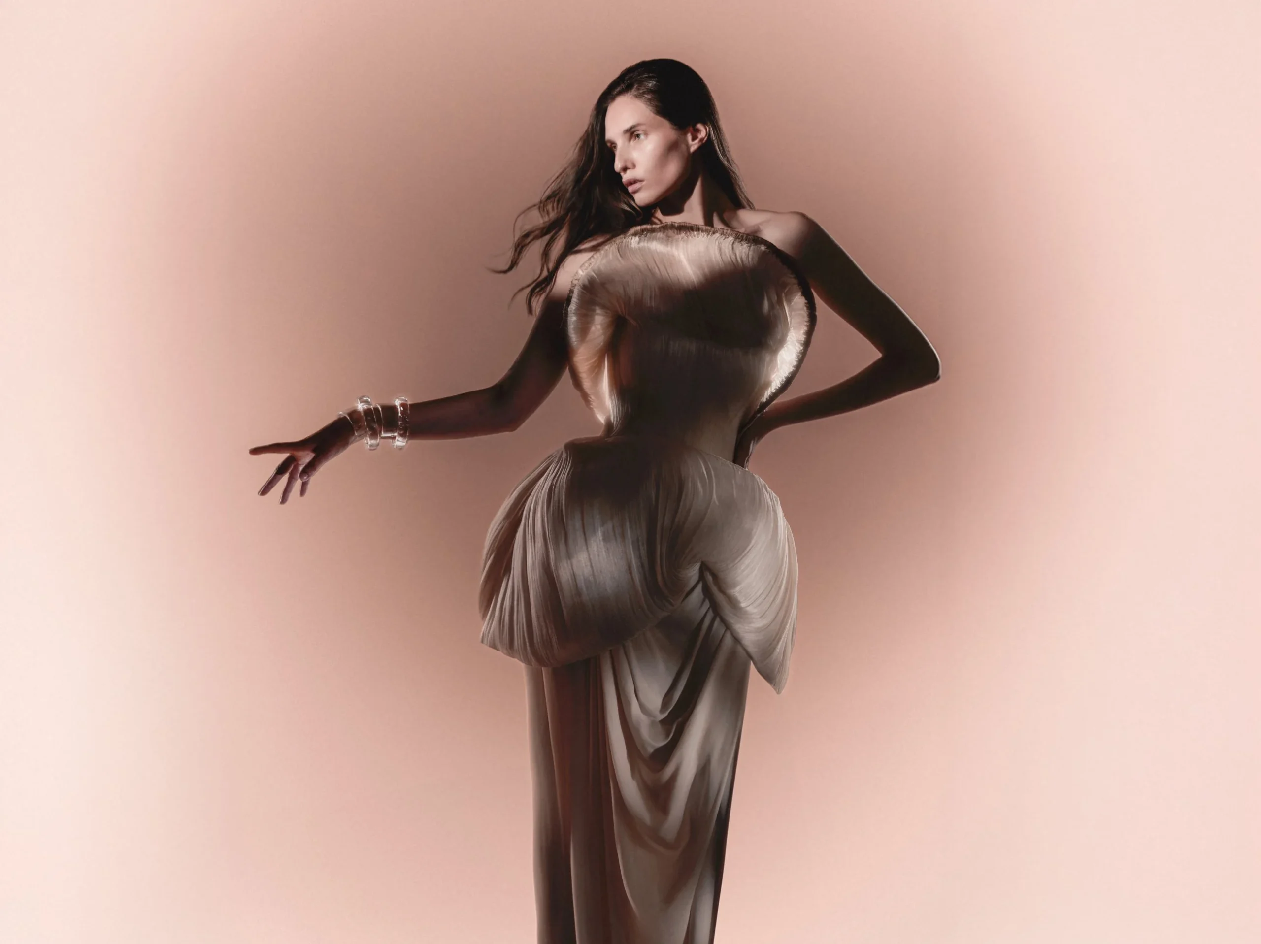 Kelsey in a sculptural pleated ivory gown with a shell-shaped bodice on a blush backdrop
